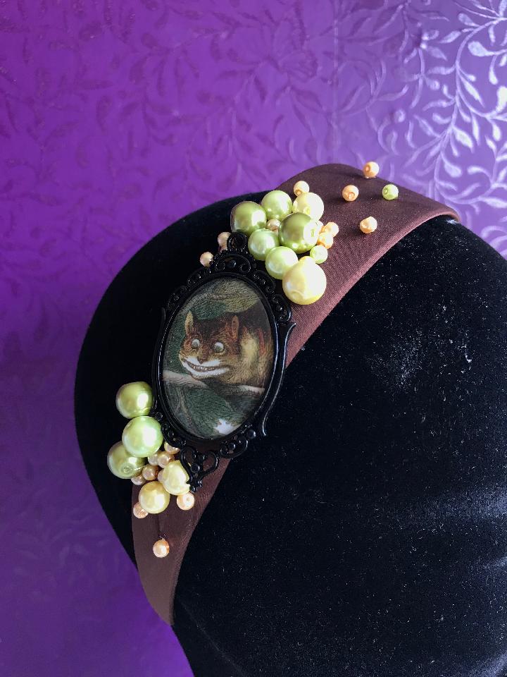 IMAGE - Brown satin headband with vintage Cheshire Cat drawing, finished with green and cream pearls.