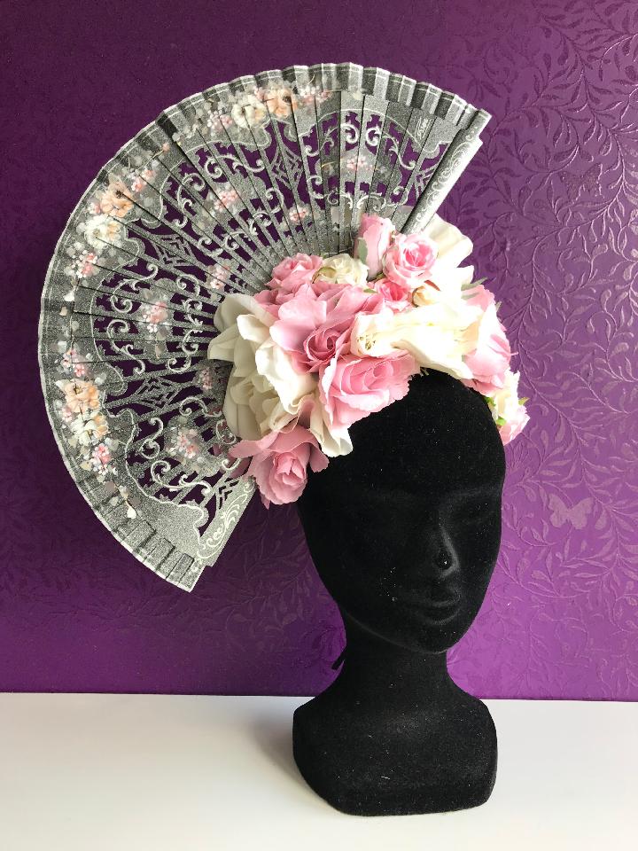 IMAGE - Black satin headband with silver painted fan. The fan has beautifuly carved shapes and is painted with pink and white flowers. The rest of the headband has pink and white roses. There is and elastic and mini comb on the inside for more comfortable wear.