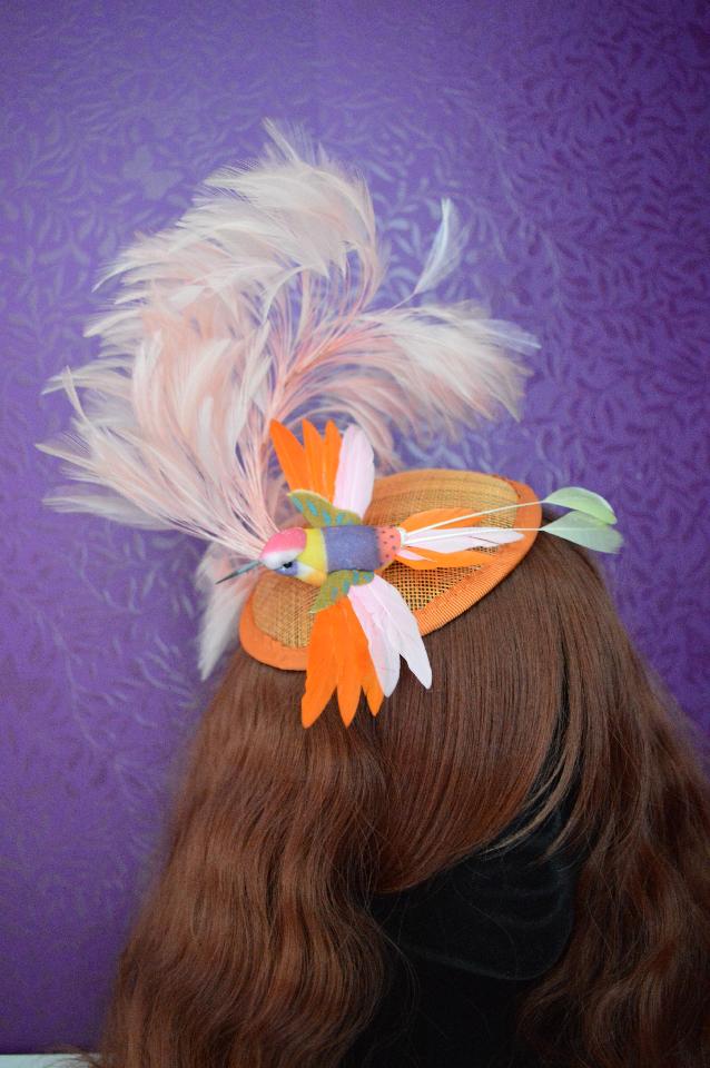 IMAGE - Orange sinamay fascinator with light pink swirly feather mount and bird. 
Fixes to hair with a comb.